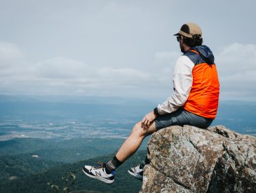 man in orange jacket sitting on rock during daytime